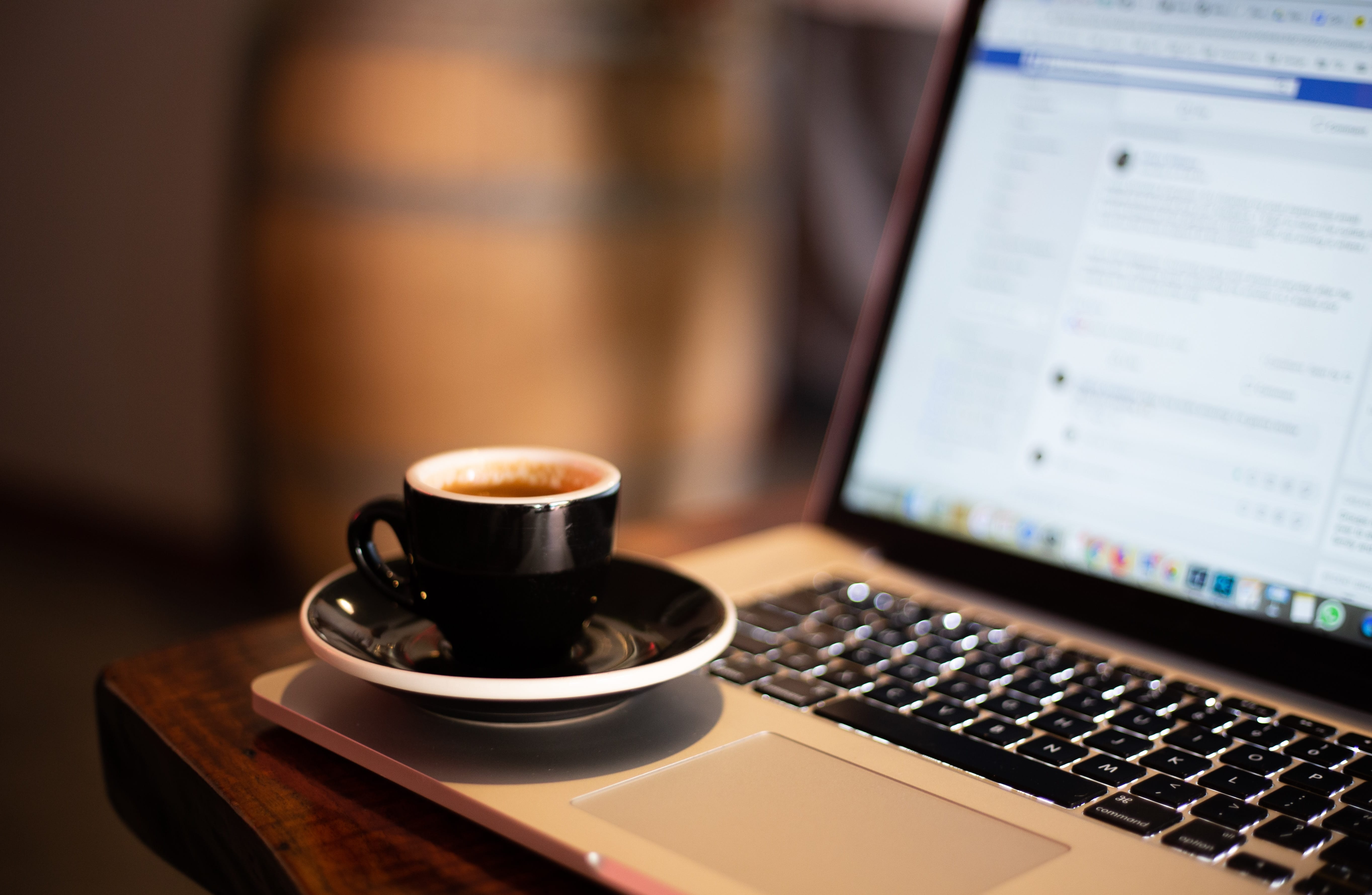 black coffee mug on laptop with facebook on screen