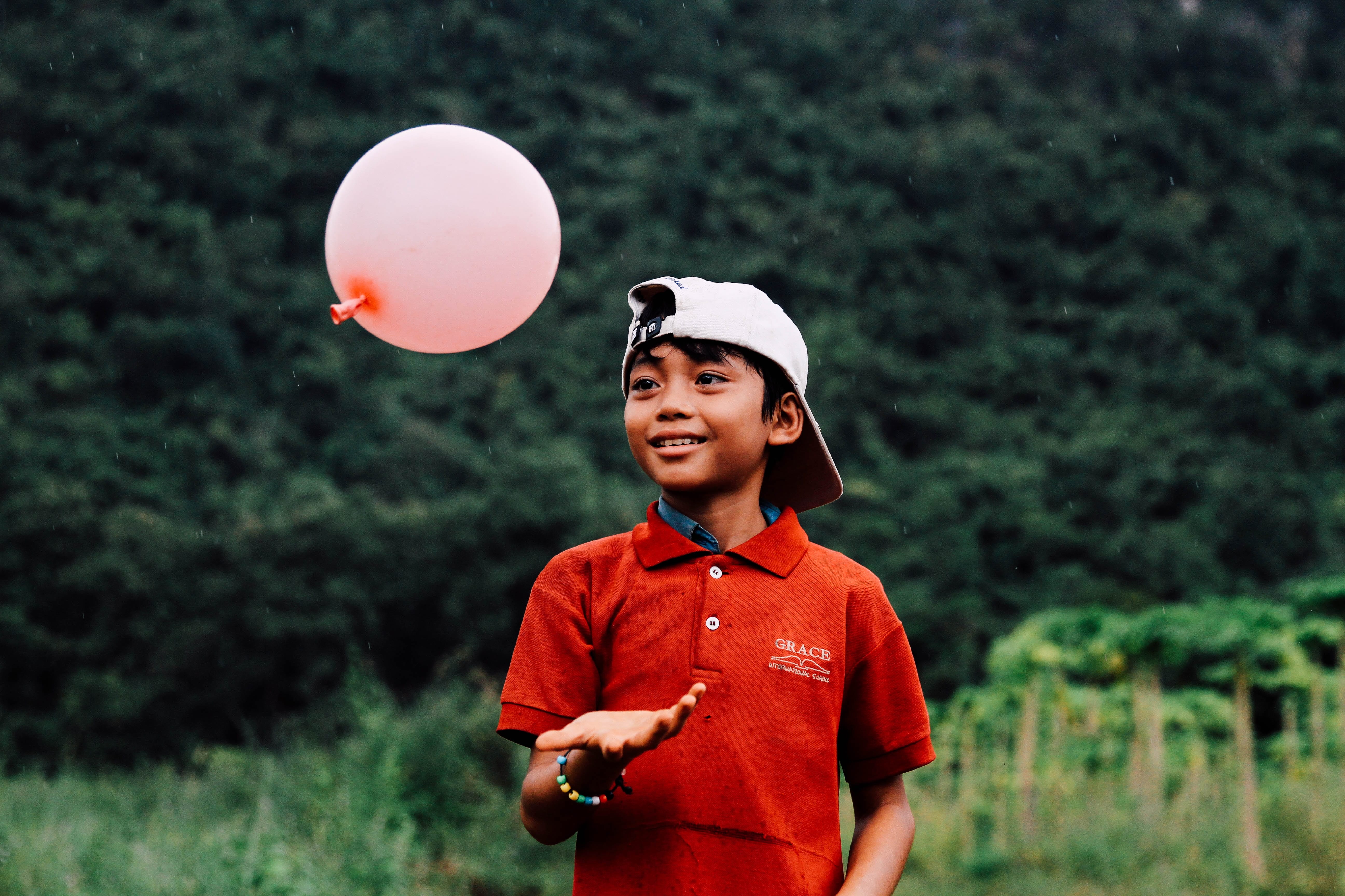 boy in red polo playing with pink balloon